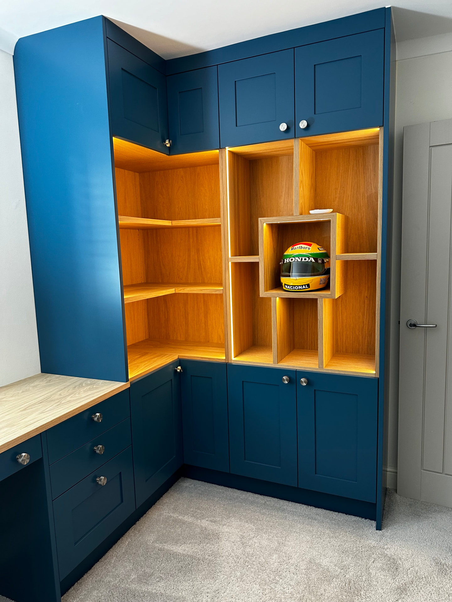 Navy blue corner office cabinetry with oak shelving, display lighting and fitted desk
