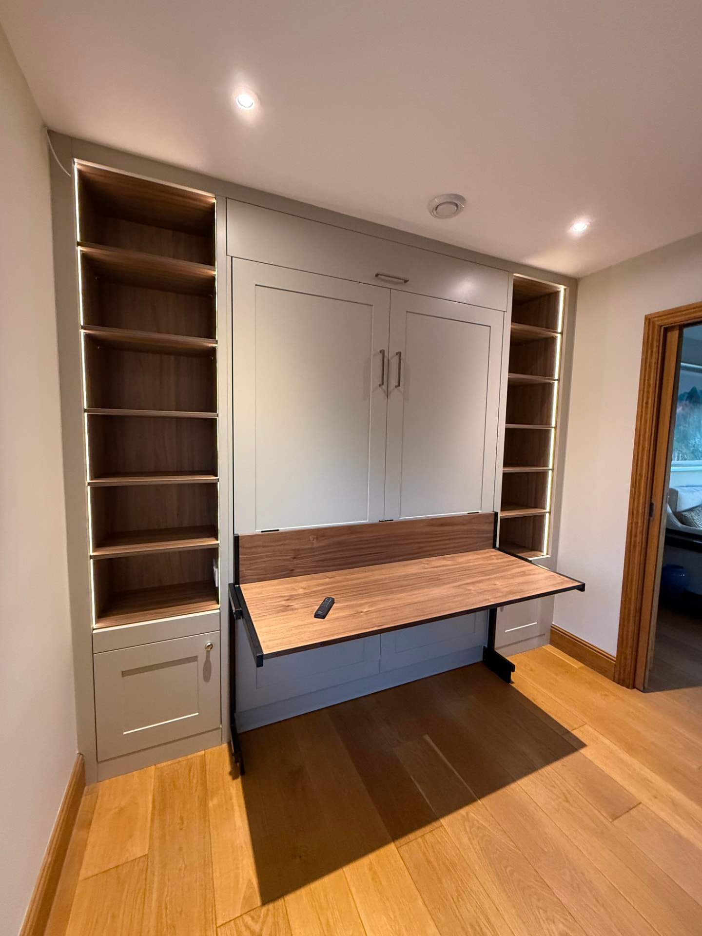 Space-saving home office with fold-down walnut desk and illuminated shelving