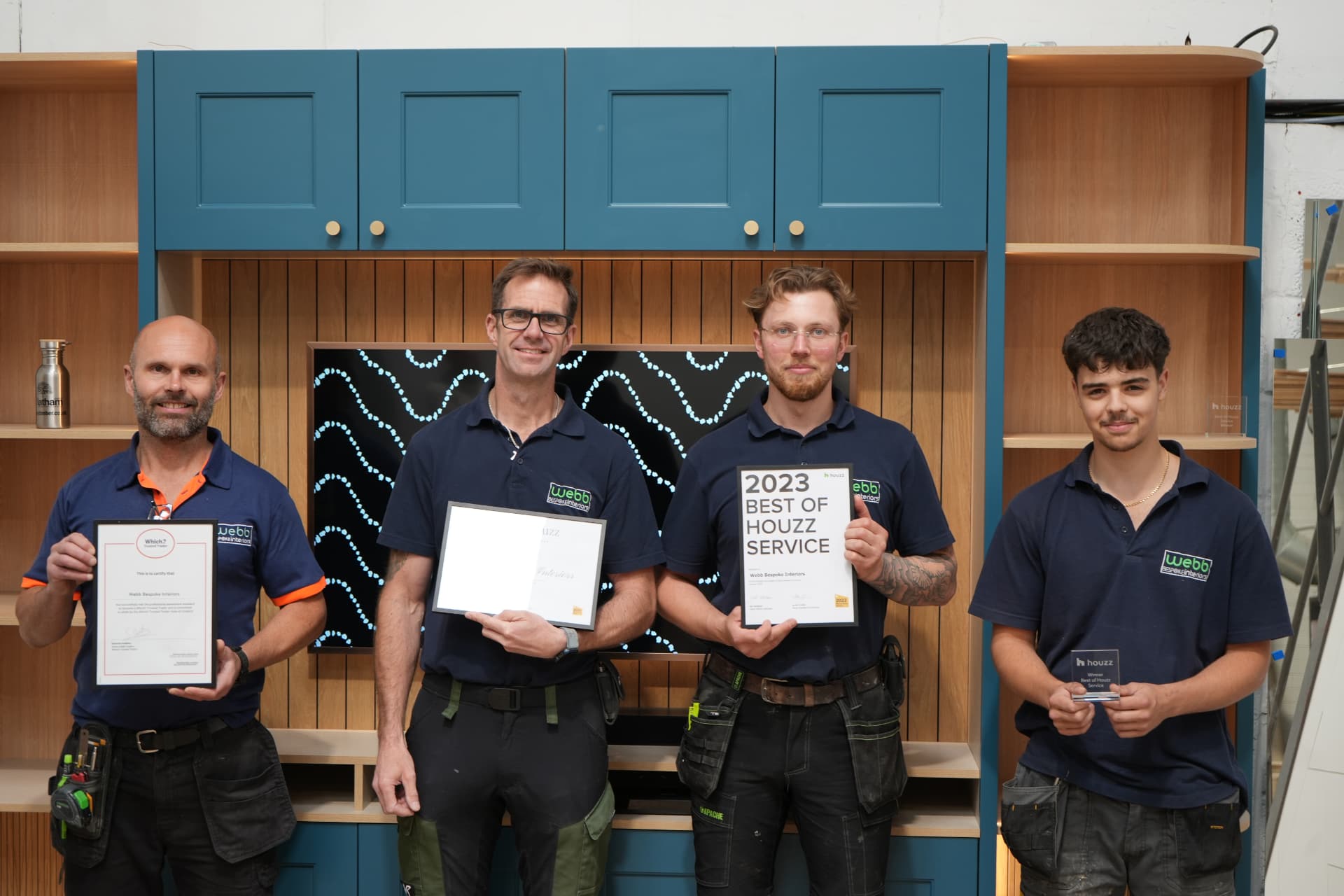 The Webb Bespoke Interiors team, four craftsmen in branded polo shirts holding their Which? Trusted Trader and Houzz awards in front of a bespoke fitted unit
